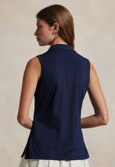 Μπλε ναυτικό αμάνικο πόλο πουκάμισο με γιακά, με λεία υφή και πλαϊνές σχισμές. Η πίσω όψη αποκαλύπτει μια εφαρμοστή σχεδίαση.