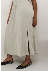 Długa, jasnoszara spódnica z przednim rozcięciem, wykonana z miękkiego materiału. W komplecie eleganckie czarne buty na szpilce z wydłużonym noskiem.