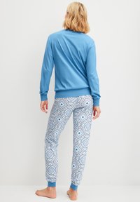  Lichtblauw langemouwen shirt met geribbelde manchetten, gecombineerd met patternd blauwe en witte pyjamabroek met bloemen- en geometrische ontwerpen.