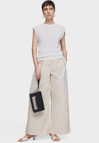White short-sleeve top paired with cream wide-leg trousers. Black handbag held with a strap. Light-colored sandals. Smooth textures.