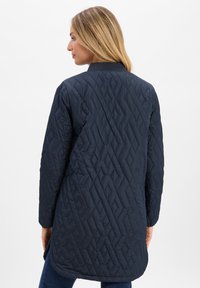 Marineblau gesteppte Jacke mit hohem Kragen, die ein Rautenmuster aufweist, lange Ärmel hat und einen etwas längeren hinteren Saum besitzt.