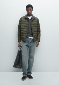 Olive green puffer jacket, gray sweater, white t-shirt, blue jeans, black suede shoes, and a dark leather tote bag. Smooth textures throughout.
