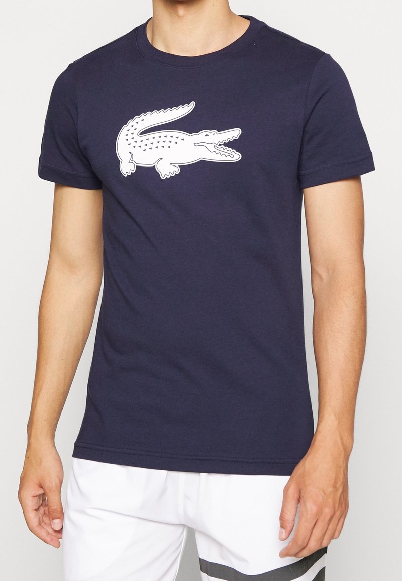 Marinblå bomull t-shirt med en vit krokodilgrafik på framsidan. Korta ärmar och rundad neckline. Designad för avslappnad användning.