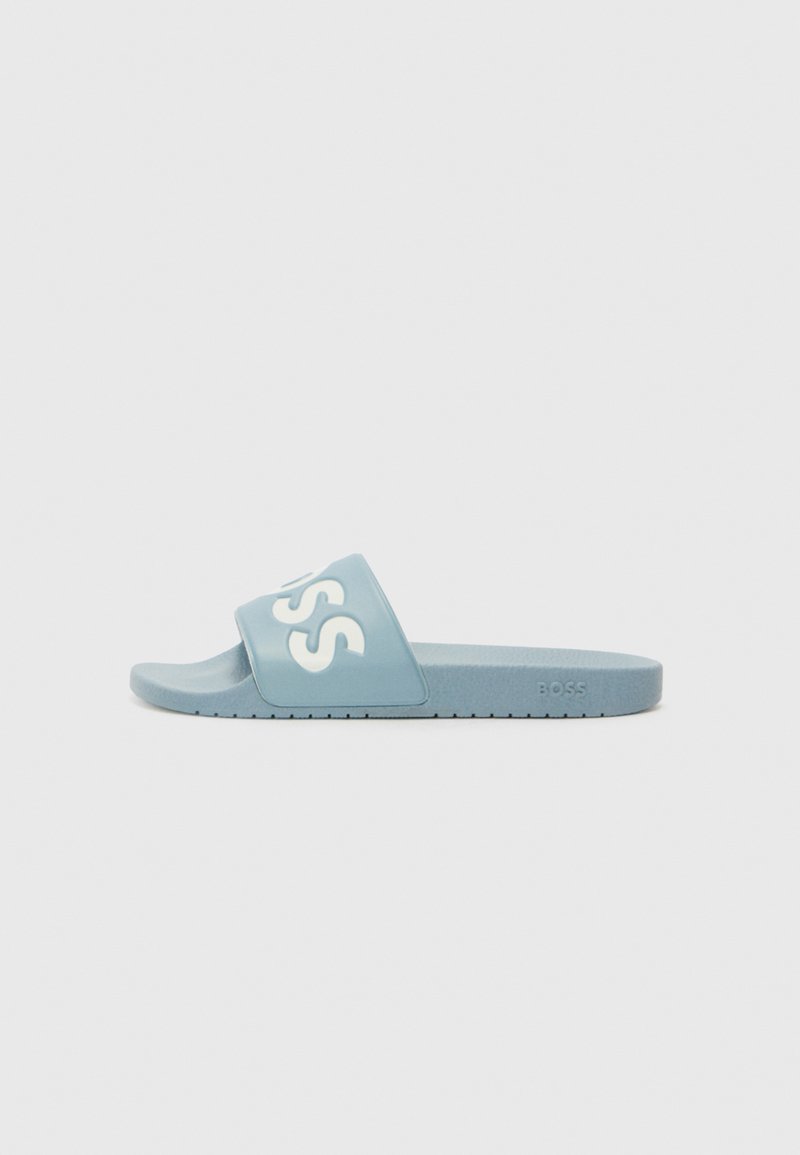 Lyseblå glidesandal laget av gummi, med en bred stropp med hvit "BOSS"-logo. Flat såle med teksturert bunn for grep.