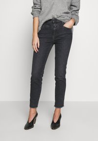 Jeans ajustados de color gris oscuro con cintura alta, mostrando un dobladillo desgastado, combinados con unos zapatos de tacón negro con acentos de tachuelas.