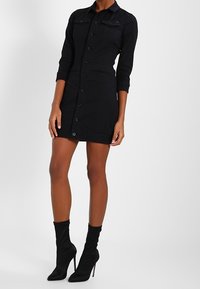 Czarna sukienka zapinana na guziki z długimi rękawami, dwoma przednimi kieszeniami i dopasowanym krojem. Do tego czarne czółenka na wysokim obcasie do kostki.