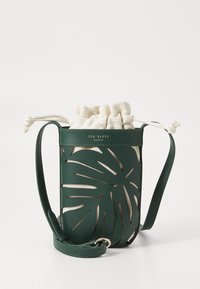 Grüne Lederhandtasche mit ausgeschnittenem Blätterdesign, innen mit einem Creme-farbenen Stoffbeutel mit Kordelzug. Inklusive Trageriemen.