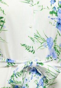 Tela blanca con estampado floral en azul y verde, con cierre de botones frontal y lazo anudado en la cintura.