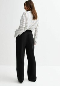Wit- en zwartgestreepte blouse met lange mouwen, gecombineerd met zwarte high-waisted broek met wijde pijpen, die een ontspannen pasvorm en een gestroomlijnd ontwerp benadrukt.