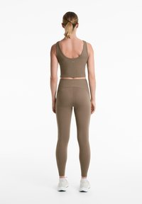 Sötétolíva zöld aktív viselet szett, amely ribbed crop topból és magas derekú leggingsből áll, sima, rugalmas textúrával és minimális márkázással.