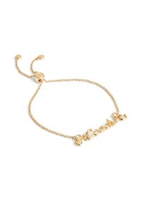 Bracelet en or avec une chaîne délicate et une plaque nominative "Coach" ornée de trois petits cristaux et de perles arrondies aux extrémités.