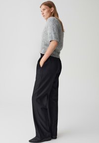 Pull court en maille grise clair et doux à manches courtes associé à un pantalon large taille haute noir. Le pantalon dispose de poches latérales et d'une coupe décontractée.