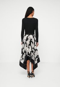 Μαύρο μπλουζάκι με μακριά μανίκια συνδυασμένο με φούστα με πτυχές σε μαύρο και άσπρο σε σχήμα ψηλού-χαμηλού, με σχέδιο φύλλων. Τα μαύρα ψηλά παπούτσια ολοκληρώνουν την εμφάνιση.