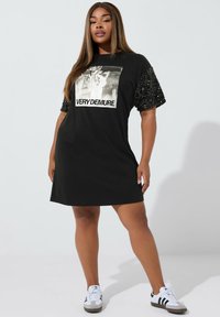 Musta puuvillamekko, jossa on lyhyet, strassikoristeiset hihat. Etupuolella on graafinen printti, jossa lukee "EHTOISEN RENNOSTI".