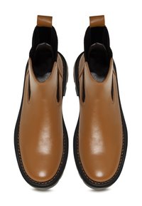 Paire de bottines Chelsea en cuir beige avec des panneaux latéraux élastiques noirs et des semelles noires épaisses, vues de dessus.