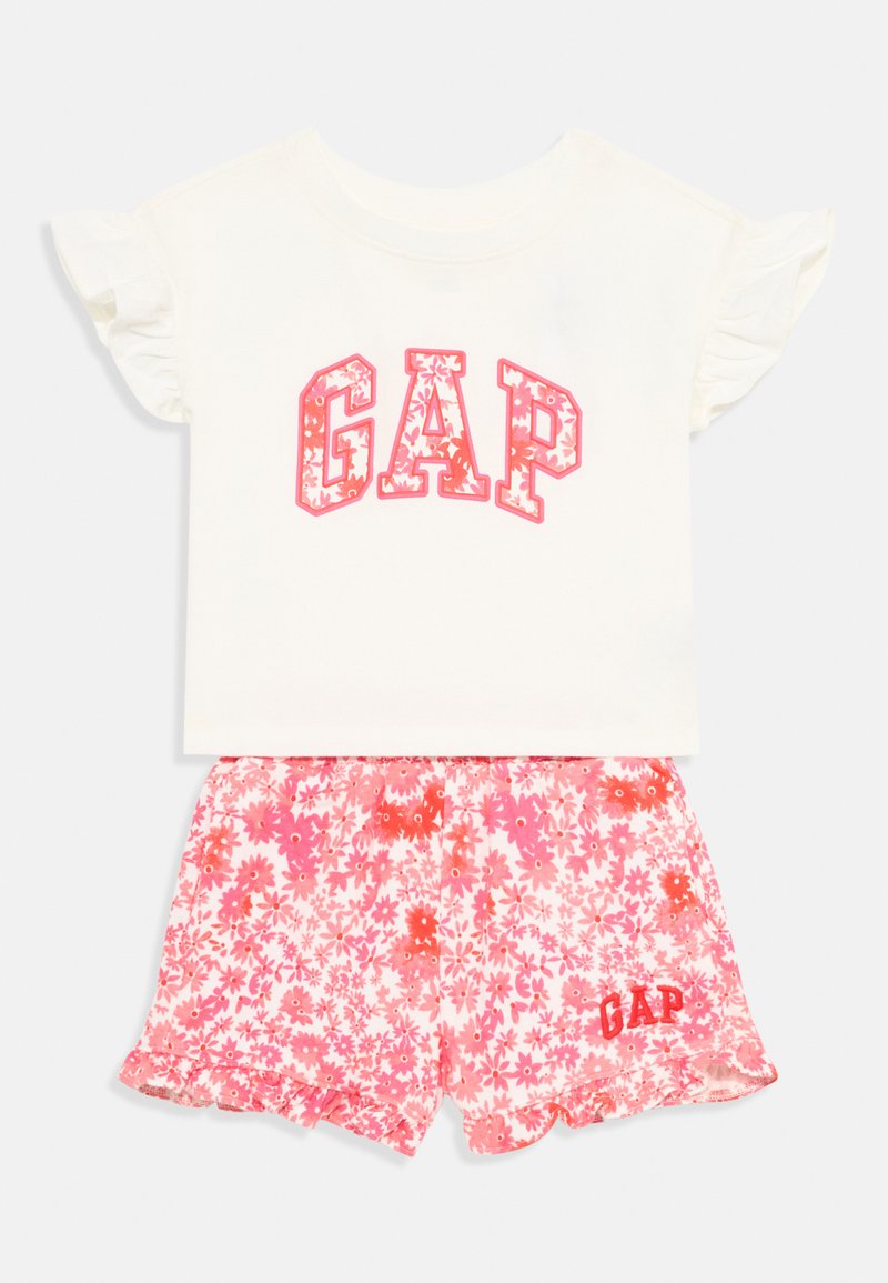 Dvoudílný outfit skládající se z bílého topu s krátkým rukávem, na kterém je růžový květinový potisk "GAP", a růžových květinových šortek s volánkovým lemem a logem.