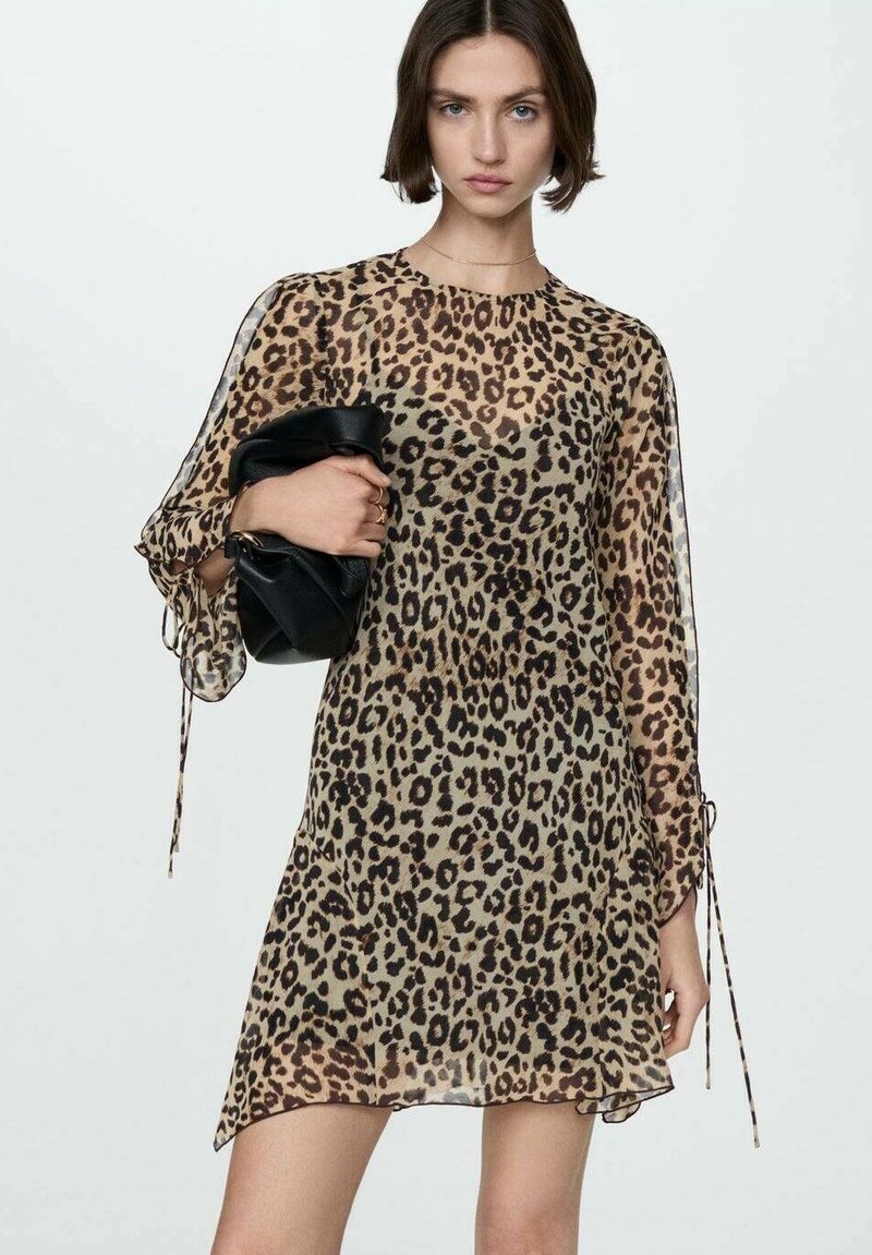 Rochie cu imprimeu de leopard, confecționată dintr-un material transparent, având mâneci lungi cu detalii legate și o croială lejeră. Este asortată cu o poșetă neagră.