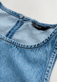 Denim-Oberteil mit rundem Halsausschnitt, hellblauer Farbe und sichtbaren Nähten. Verfügt über einen Verschluss auf der Rückseite und ein "NEXT"-Etikett.