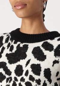 Black and white leopard print sweater with a ribbed black neckline, featuring a textured fabric and bold animal patterns.