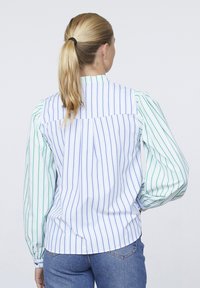 Stribet skjorte med vertikale blå og grønne striber, puffede lange ærmer og en let høj-lav kant. Lavet af et letvægtsstof.