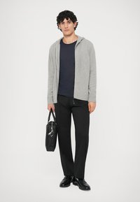 Pelēkas adītas kapuces džemperis, tumši zils T-krekls, melnas bikses un melni apavi. Tur melnu somu ar metāla detaļām. Vienkāršs, mūsdienīgs dizains.