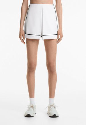 Vita skräddarsydda shorts med svarta detaljer, slät tyg, plisserad front och rak fåll. Bärs med vita sneakers och strumpor.