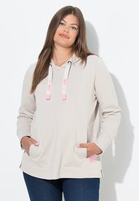 Hoodie beige realizzato in tessuto morbido, con cappuccio regolabile, tasche frontali e un dettaglio del logo rosa sull'orlo. Maniche lunghe e vestibilità rilassata.