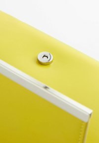 Petit sac jaune avec un bouton-pression magnétique argenté et une bordure argentée sur le bord, sur fond blanc.