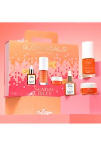 Zestaw pięciu produktów do pielęgnacji skóry od Sunday Riley, z pomarańczowym i białym opakowaniem na jasnoróżowym gradientowym tle.