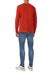 Langärmliges rotes Baumwoll-T-Shirt mit Rundhalsausschnitt, kombiniert mit hellblauen Slim-Fit-Jeans und weißen Sneakers mit grünen Akzenten.