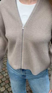 Sweat à zip avec texture côtelée en beige clair, doté d'une fermeture éclair argentée et d'un t-shirt blanc en dessous, associé à un jean bleu.