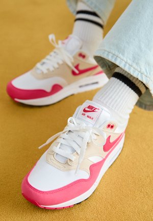 Weiße und rosa Nike Air Max Sneakers mit einem beigen Obermaterial, das über eine strukturierte Oberfläche verfügt, weißen Schnürsenkeln und einer sichtbaren Air-Sohle.