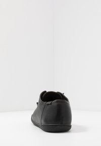 Zapato de cuero negro con una textura suave, forma redondeada, perfil bajo y diseño minimalista. Presenta un sutil detalle de costura y un forro suave.