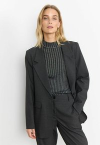 Dunkelgrauer Blazer mit spitzen Revers, kombiniert mit einem taillierten schwarz-silbernen gerippten Pullover. Taillierte Passform mit aufgesetzten Taschen und einem Knopfverschluss.