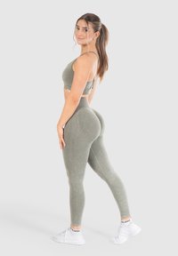 Set sportivo abbinato di reggiseno e leggings color verde oliva con una texture liscia, design aderente e dettagli di cucitura sottili, abbinato a scarpe da ginnastica bianche.