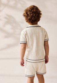 Korte, cremefarvede sæt af struktureret stof bestående af en kortærmet top med krave og matchende shorts, fremhævet med mørkeblå striber.