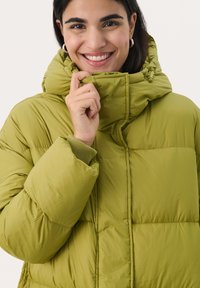 Groene pufferjack met een hoge kraag, met doorgestikte secties en ribgebreide manchetten. Het materiaal lijkt soepel en geïsoleerd.