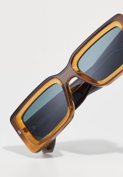 Brown oversized sunglasses with a transparent amber frame, rectangular shape, dark lenses, and minimal hardware accents.