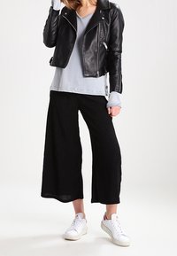 Giacca da moto in pelle nera, t-shirt a maniche corte grigia chiara con scollo a V, pantaloni neri a gamba larga e scarpe da ginnastica bianche con dettagli rossi. Tessuto strutturato e zip.
