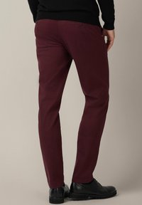 Burgundowe spodnie dresowe o dopasowanym kroju, z dwiema tylnymi kieszeniami z guzikami i szczegółowym przeszyciem, w zestawie z czarnymi butami eleganckimi.