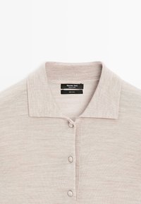 Jasnobeżowa wełniana koszulka polo z klasycznym kołnierzykiem, listwą z guzikami oraz żebrowanymi detalami wzdłuż krawędzi kołnierzyka i listwy.