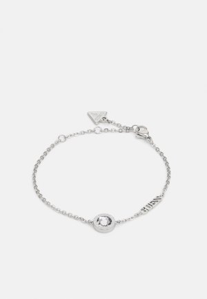 Pulseira de corrente de prata com um cristal claro central, com um suporte texturizado e uma pequena etiqueta de marca com a palavra "GUESS."
