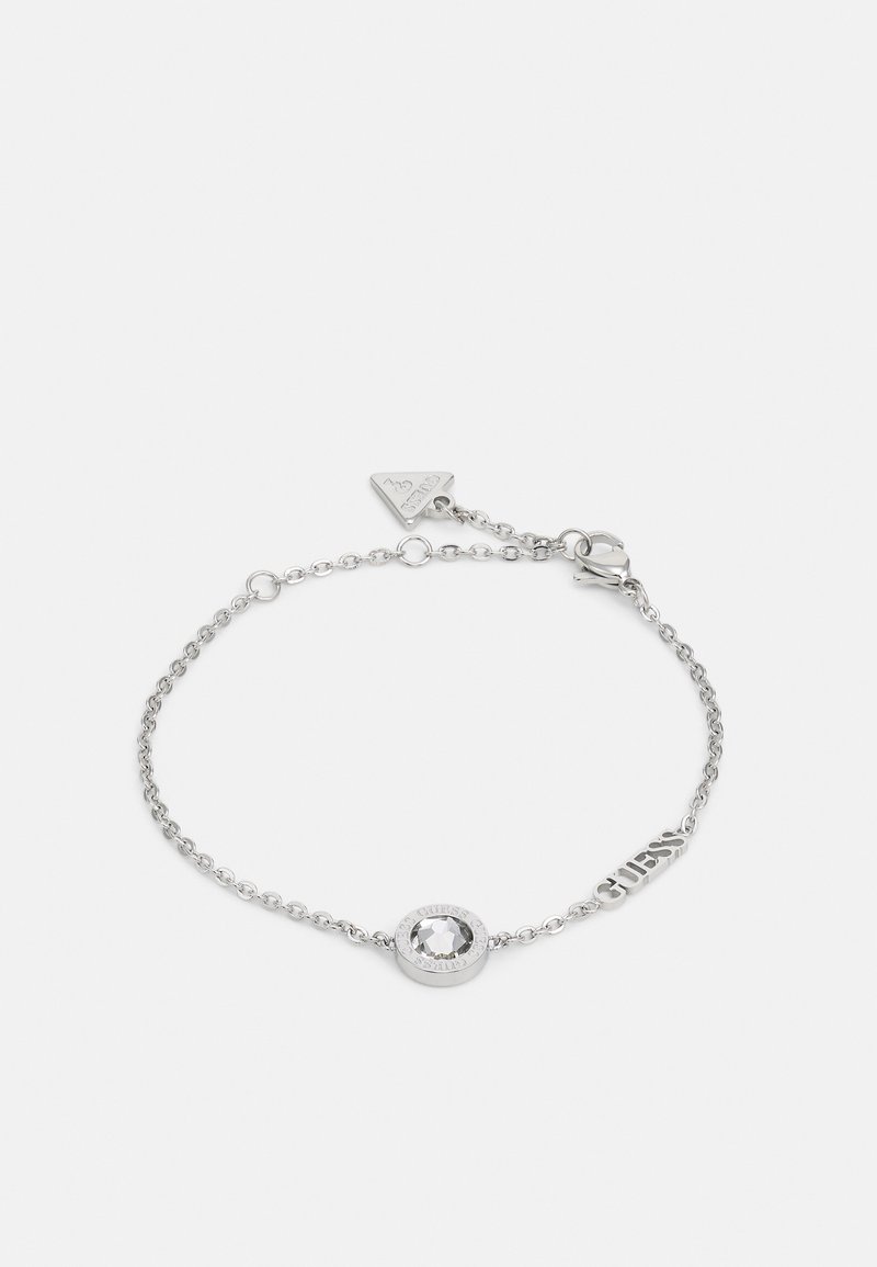 Silberne Kettenarmband mit einem zentralen klaren Kristall, der in einer strukturierten Fassung eingesetzt ist, sowie einem kleinen Markenanhänger mit dem Wort "GUESS."