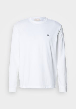 T-shirt bianco a maniche lunghe in cotone, con scollatura rotonda e un piccolo logo nero "CK" sul lato sinistro del petto.