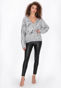 Srebrny sweter z cekinami, z dekoltem w kształcie V, luźny krój i długie rękawy. Połączony z czarnymi skórzanymi legginsami i sandałami na wysokim obcasie.