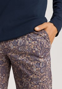 Mörkblå långärmad skjorta med slät yta, i kombination med ljusbruna byxor som har ett detaljerat mörkblått paisleymönster och blommiga inslag.