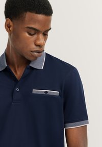Polo navy con collo a righe e dettaglio tasca, dotato di abbottonatura a due bottoni e maniche corte con polsini a righe.