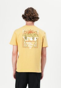 Gul bomulls T-skjorte med et fargerikt grafisk motiv på ryggen med fjell, kaktuser og en sol, merket med "Quiksilver."