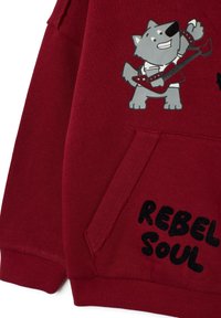 Rode sweatshirt met een grafisch ontwerp van een cartoonwolf die gitaar speelt, met zwarte tekst "REBEL SOUL" nabij de zak. Zacht, textuurstof.