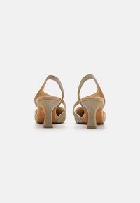 Sandales à talons beiges en tissu scintillant, avec un design à dos ouvert et un talon bloc. Doublure intérieure douce et matériau extérieur texturé.